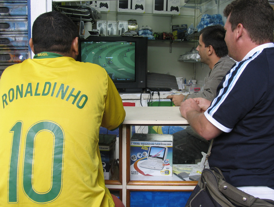  Футбольные фанаты повторяют на PlayStation 2 матч Бразилия — Гана в одной из палаток на рынке в Рио-де-Жанейро. Сборные двух стран встречались в ⅛ финала на чемпионате мира в 2006 году. Бразильцы выиграли со счётом 3:0. Фото Flickr/Paul Keller